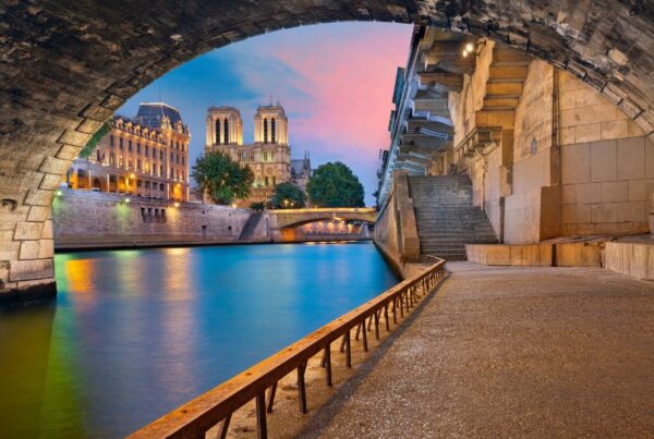 This is an image of the Seine from under a beautiful tunnel. You can see the Notre Dame in the distance and the sunset is reflecting pink on to the water.
