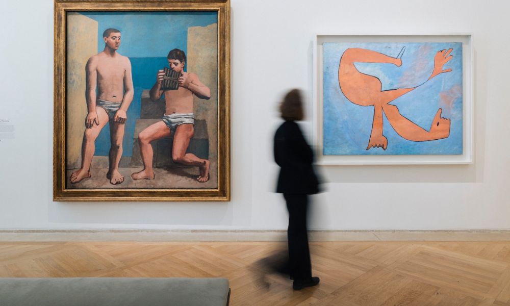 This is an image of a wall with two big frames hung up on to it and a lady walking past.