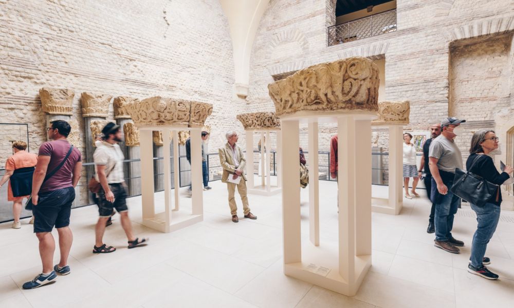 This is an image of a big room with sandstone walls and people milling around looking at ancient ruins.