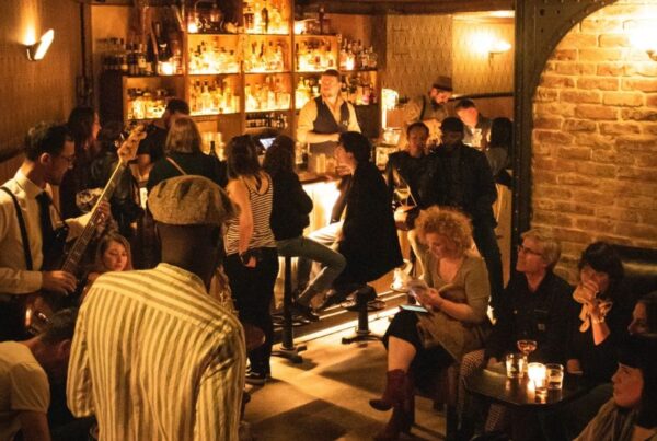 This is an image of a bar with people mingling around. There is low lighting anf brick walls.