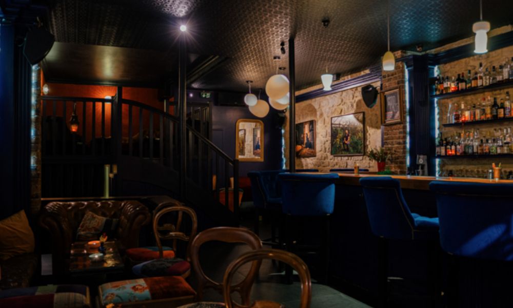 This is an image of a dark speakeasy with a bar and low lighting, plus lots of comfy chairs.