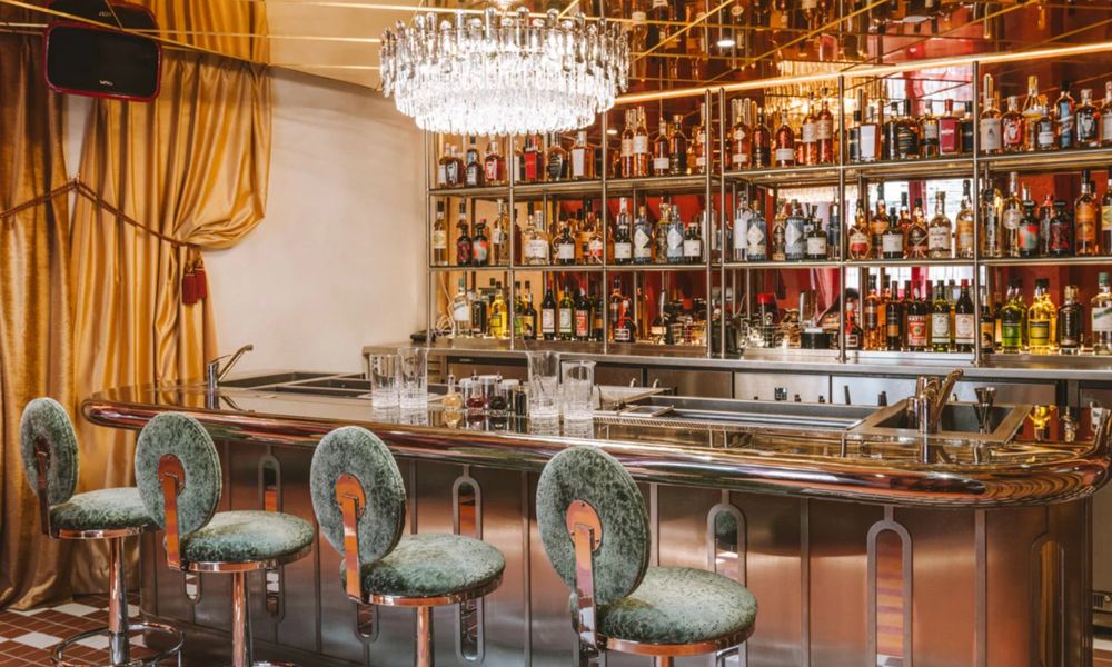 This is an image of a clean cut bar with a chandelier and plush seating.