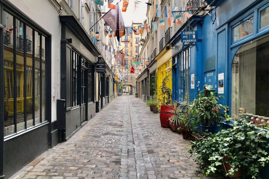 This is an image of a lively cobblestone street with flags hung up in the middle and fun-coloured stores lining the sides.