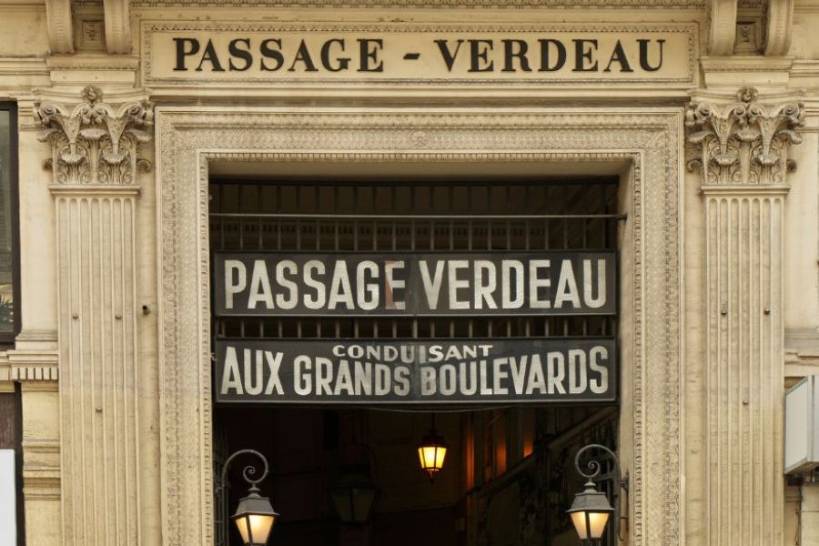 This is an image of a passageway with a big sign saying Passage Verdeau and two lamp posts at its entrance.