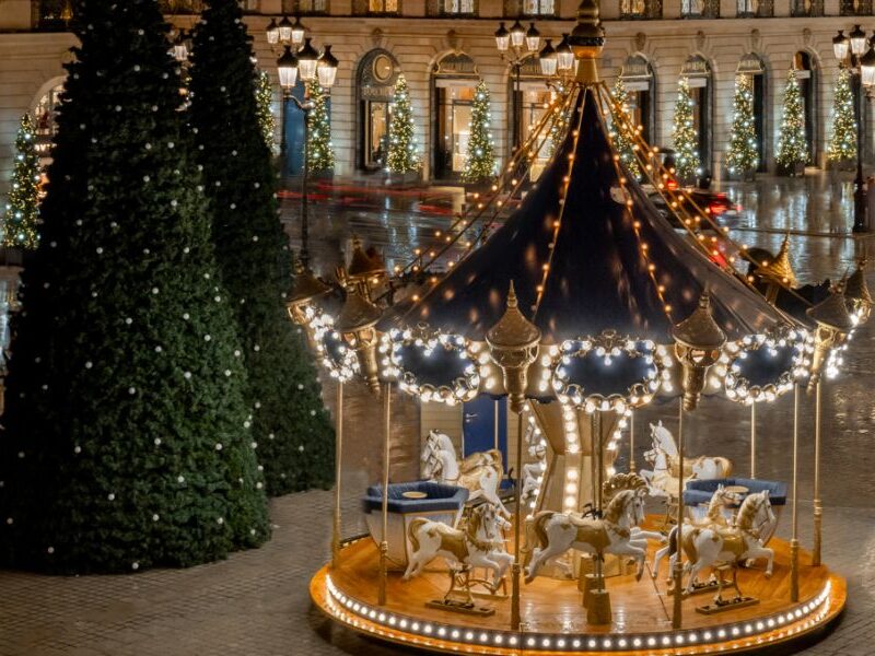 This is an image of a super Chrismassy Square out front of the Ritz in Paris with lit-up Christmas trees and a decorated merry-go-round.