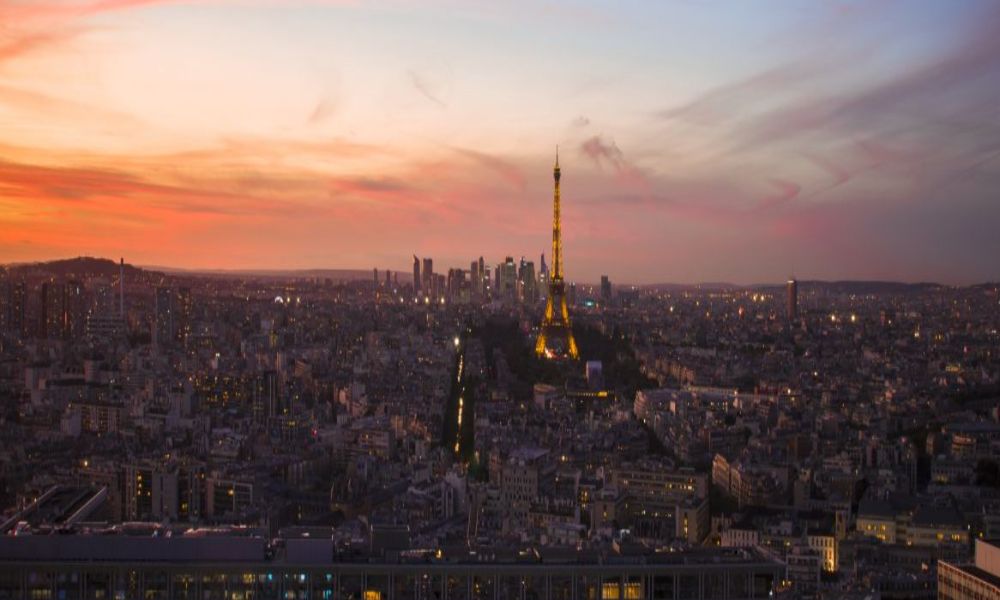 This is an image of Paris from above with a lit-up, sparkling Eiffel Tower in the centre. There is also a wonderful pink sunset in the distance.