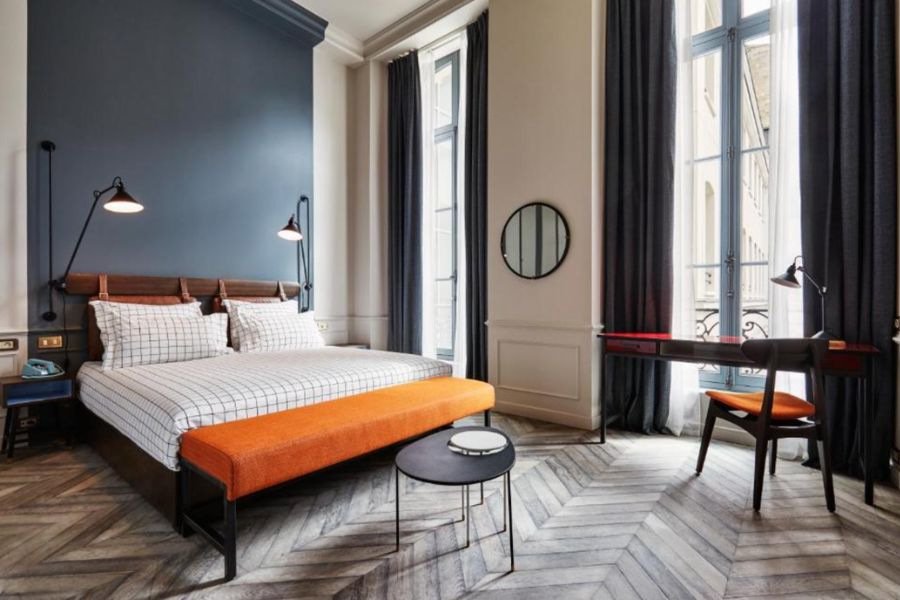 This is an image of a hotel with a lot of light streaming in, tall ceilings and a double bed with lamps overlooking the beds.