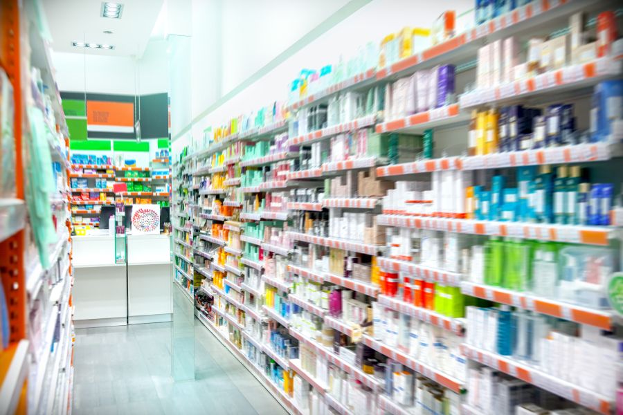 A brightly lit pharmacy aisle lined floor-to-ceiling with colourful skincare and healthcare products on both sides, with a slight soft-focus effect giving the scene a sense of abundance.