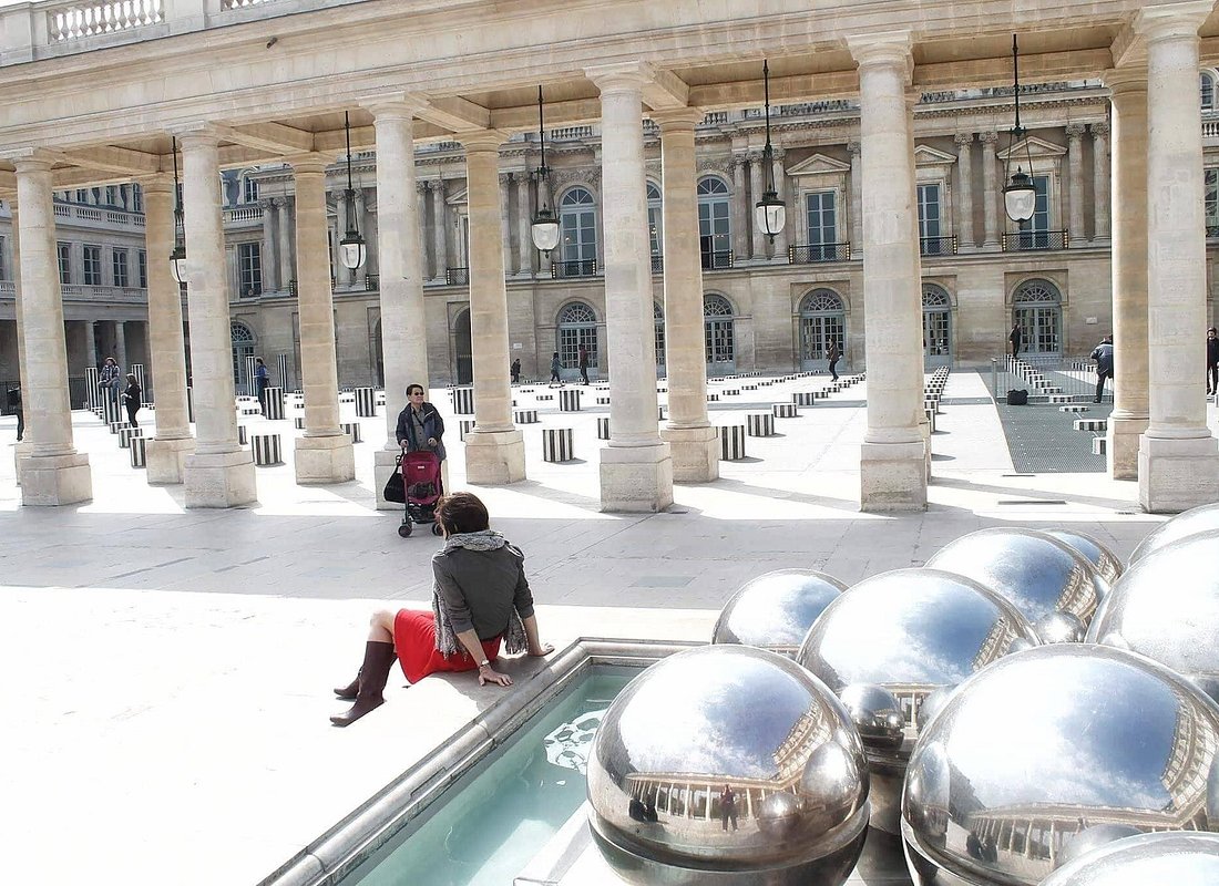 A person sitting by a metal circular sculpture, outside a museum.