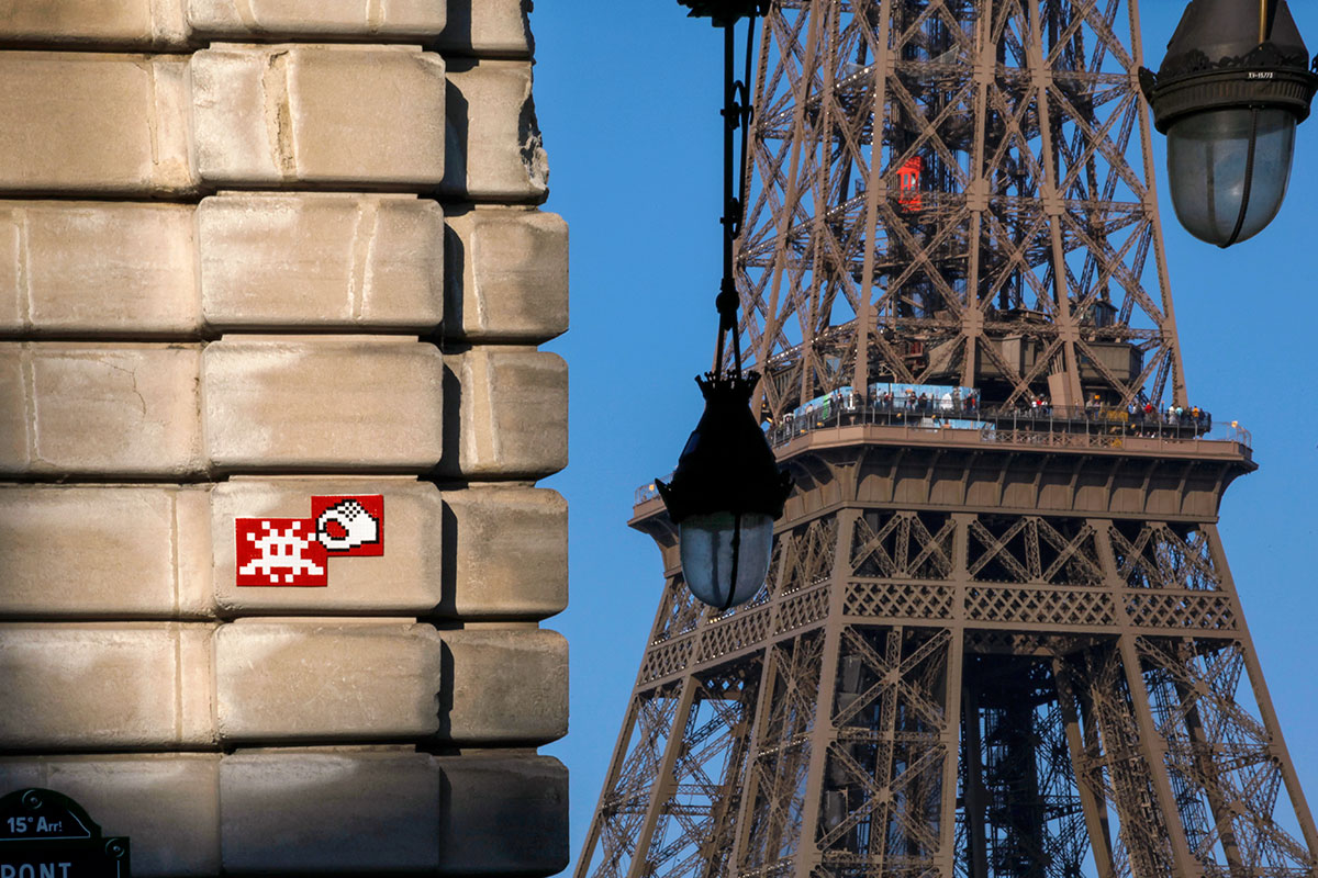 A small street art piece on a wall. The Eiffel Tower is in the background of the image.