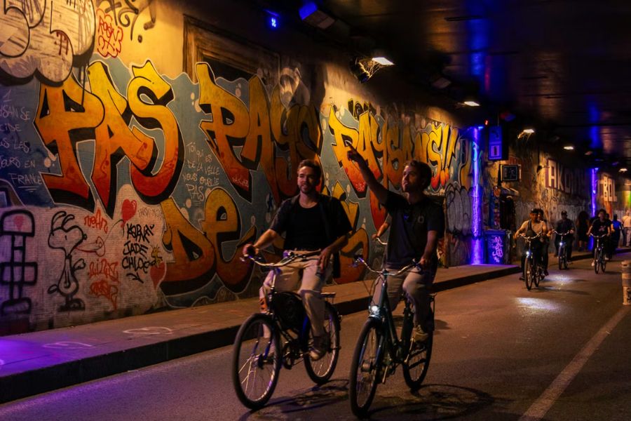 This is an image of people riding their bike through a graffitied alley way.