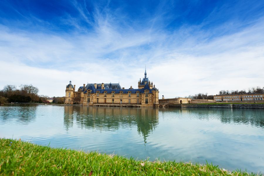 This is an image of a castle in Chantilly across from a blue lake.