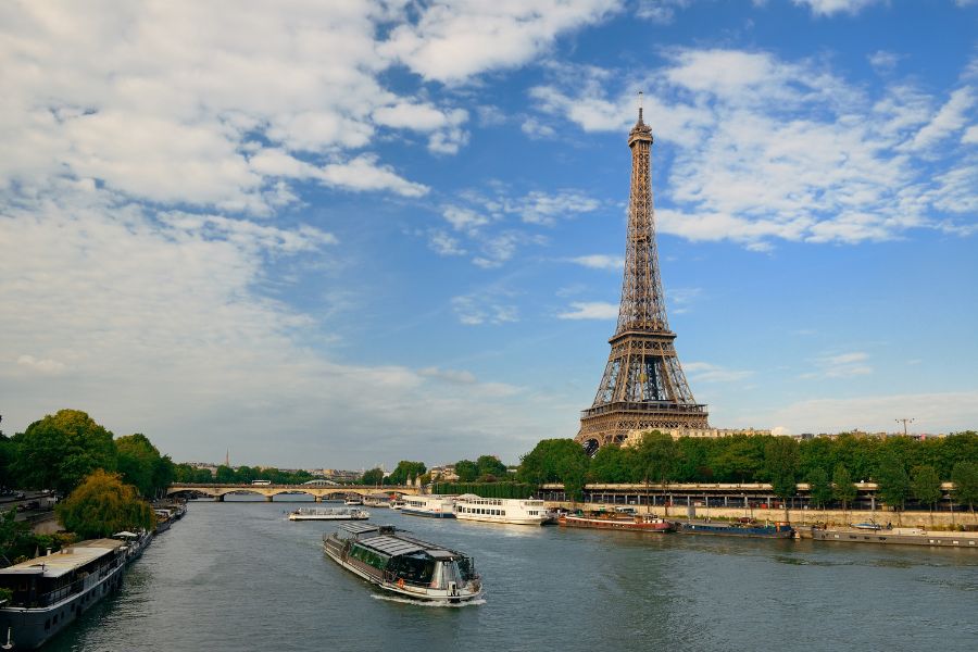 This is an image of the Seine. There is a boat strolling through and the Eiffel Tower is behind in the near distance.