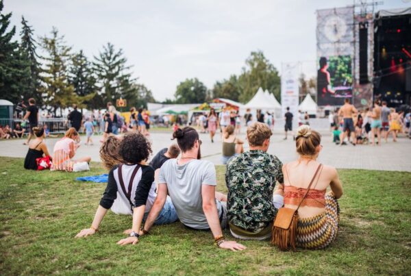 This is an image of a summer festival where four friends are sitting down watching the stage and all the stalls around it.