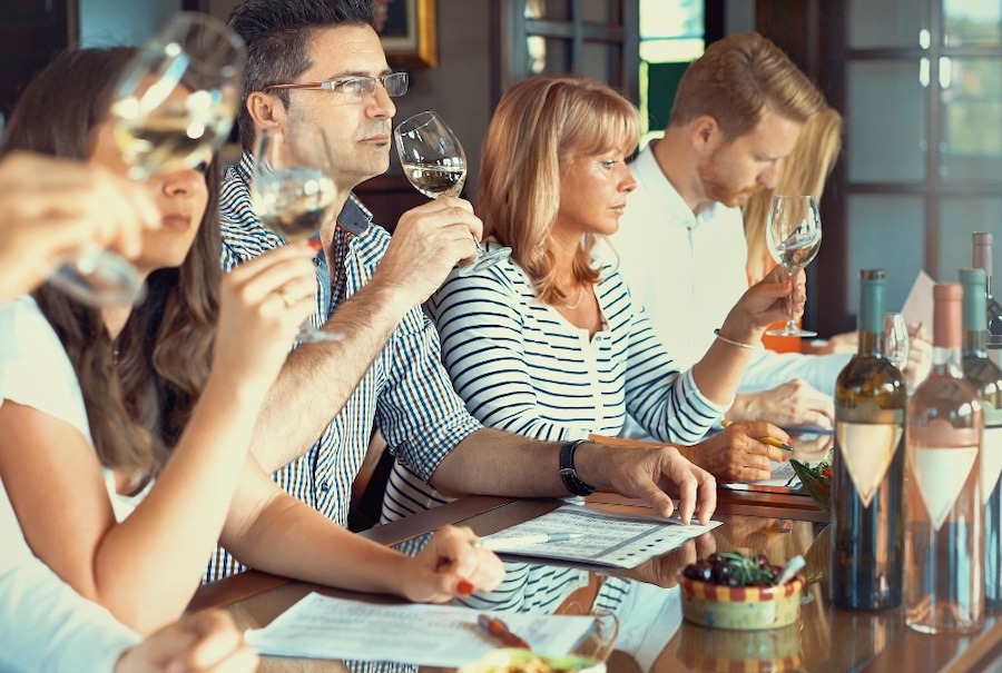 A close-up side view shows a group of adults tasting different wines at a local winery.