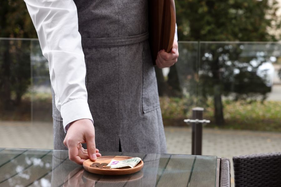 This is an image of a waiter picking up a plate of tips from a table.