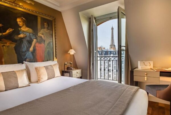 This is an image of a large king bed against a feature wall that's been painted with renaissance art. To the right, there is also a big door that opens out to an Eiffel Tower view.