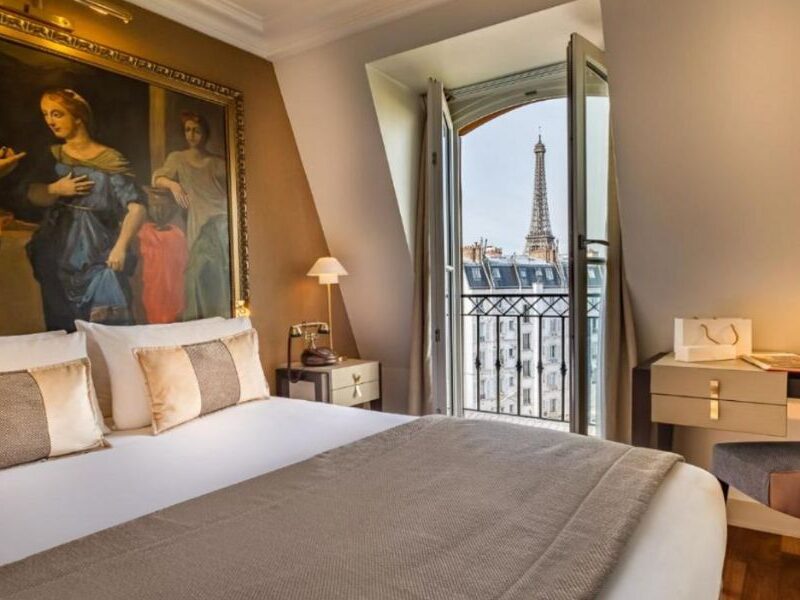 This is an image of a large king bed against a feature wall that's been painted with renaissance art. To the right, there is also a big door that opens out to an Eiffel Tower view.