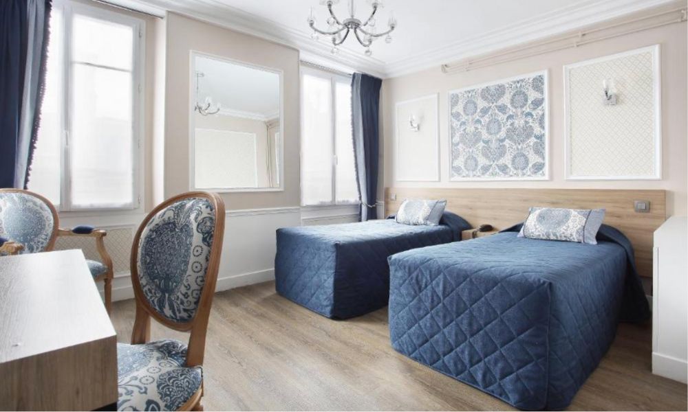 This is an image of a simple, minimalist hotel room with two single beds, a chair and several large windows.