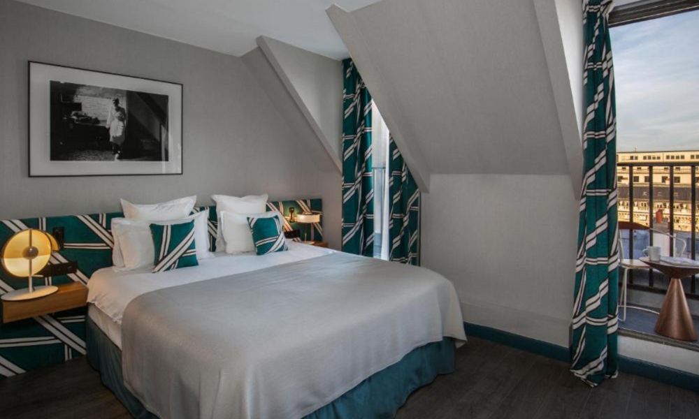 This is an image of a large double bed with a door that leans out to a balcony with a beautiful Louvre view.