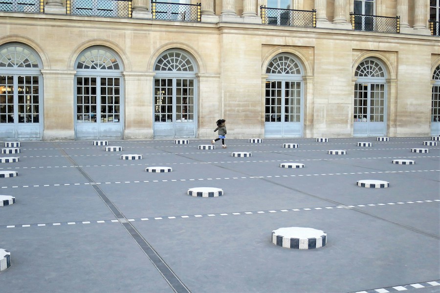 This is an image of an art installation in a courtyard in Paris which has a bunch of large bollards kids can climb on and take photos with. The bollards are black and white and distributed throughout the whole area
