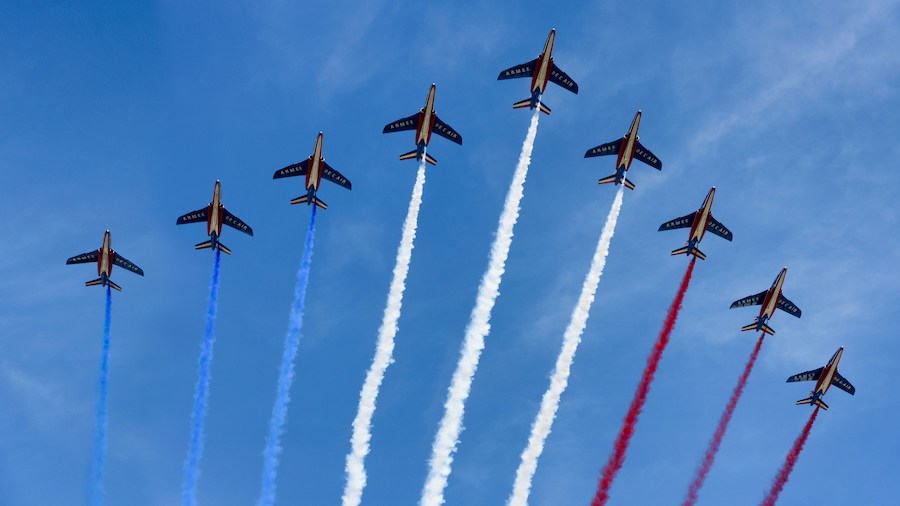 This is an image of fighter jets flying overhead with red, blue and white smoke.