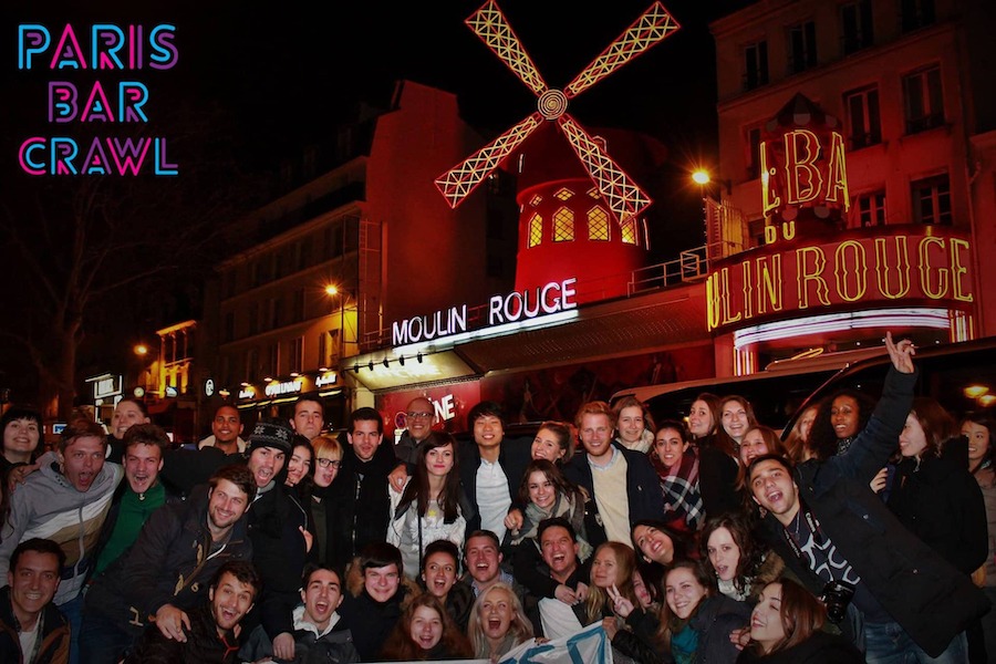 This is an image of a bar crawl in Paris full of people looking like they are having fun. The Moulin Rouge is in the background.