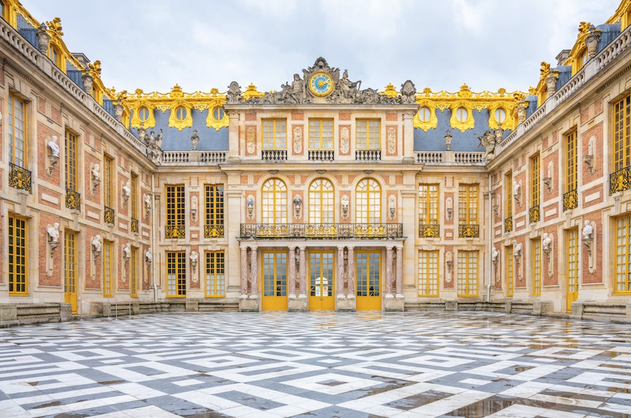 This is an image of the facade of the Palace of Versailles. The building is grand with lots of gold features.