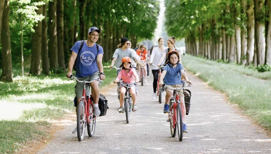 This is an image of a a group riding bikes through a green area on a path. There are both adults and children.