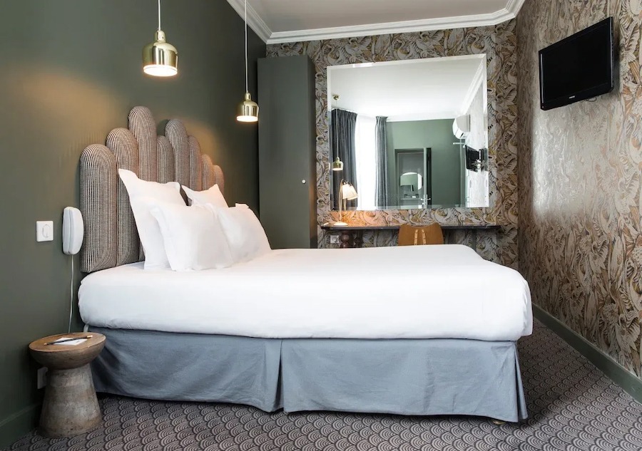 This is an image of a hotel bedroom with a big double bed dressed in white sheets. The rest of the room is toned in muted colours like beige and brown.