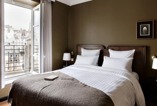 This is an image of a bright hotel room with open windows and a big double bed and brown walls.
