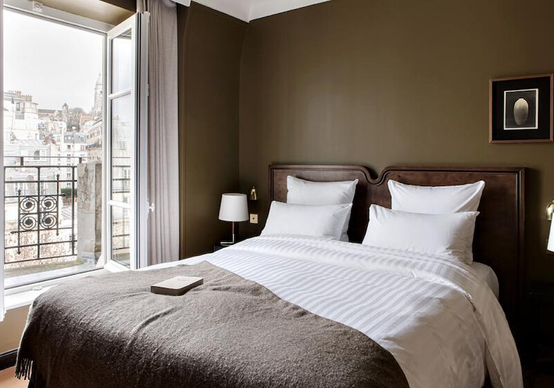 This is an image of a bright hotel room with open windows and a big double bed and brown walls.