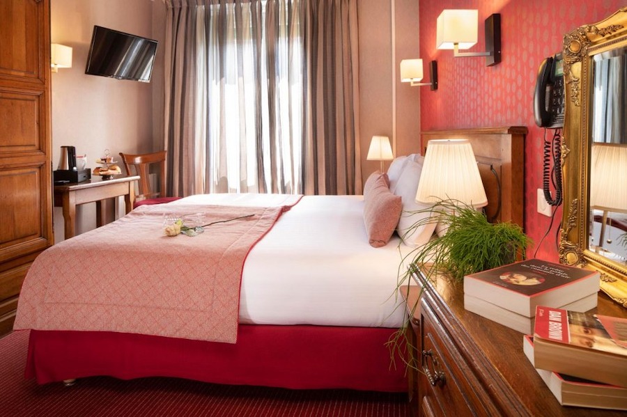 Budget Friendly Hotels In Paris with a pink vibe. Bothe the walls and the bed are salmon pink, with white bedsheets and a nice bright window.