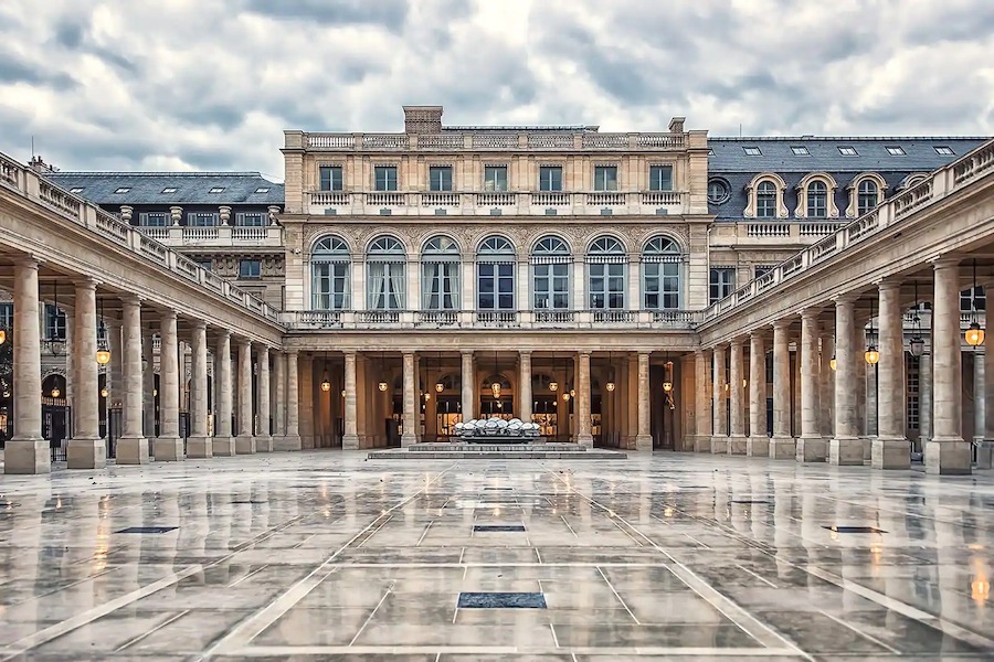 This is an image of the facade of a grand museum in Paris with stone light grey walls and a pristine and shiny front courtyard.