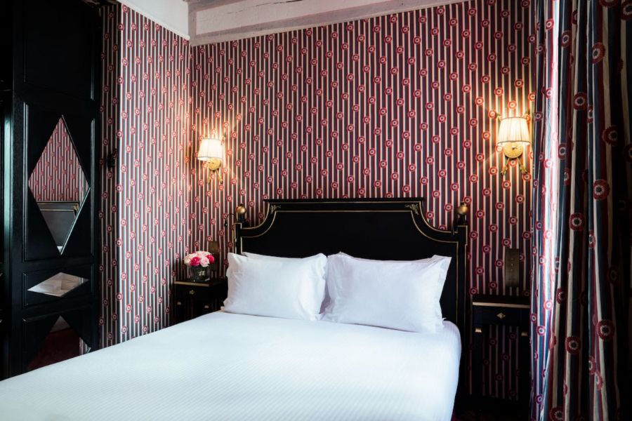 Cool Hotels In The Marais Paris: This is an image of a large hotel room with a red feature wall. The double bed has a white duvet.