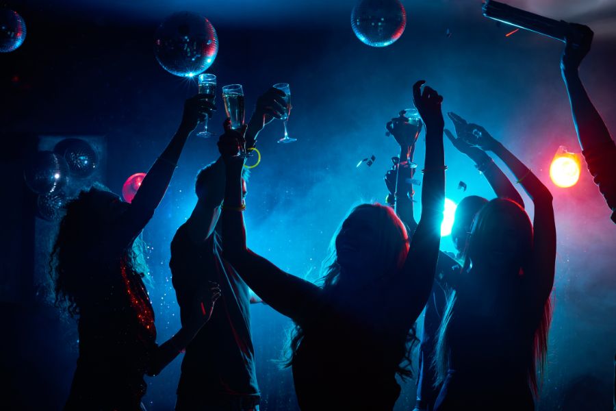 This is an image of silhouettes dancing in a dark bar with disco balls and drinks in the air.