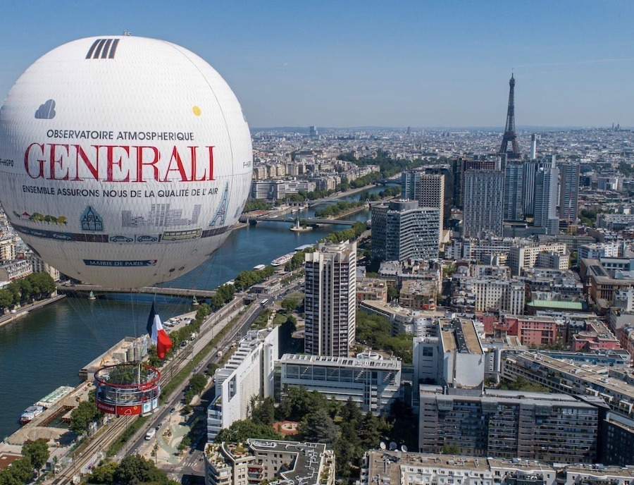 This is an image of a hot air balloon flying over a birds-eye view of Paris. You can see the Seine and the Eiffel Tower in the distance.