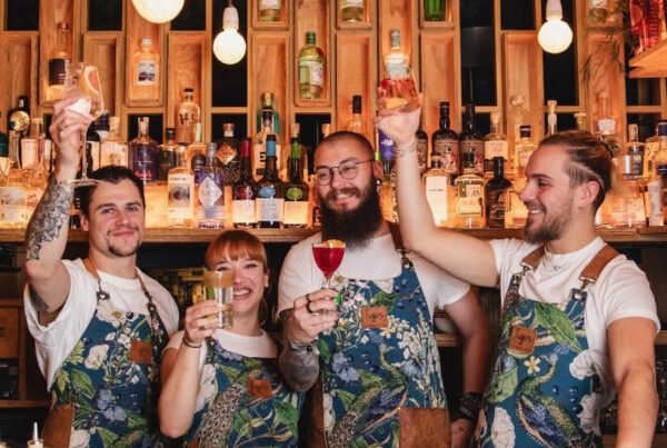 This is an image of a group of people behind a bar holding cocktails and smiling.
