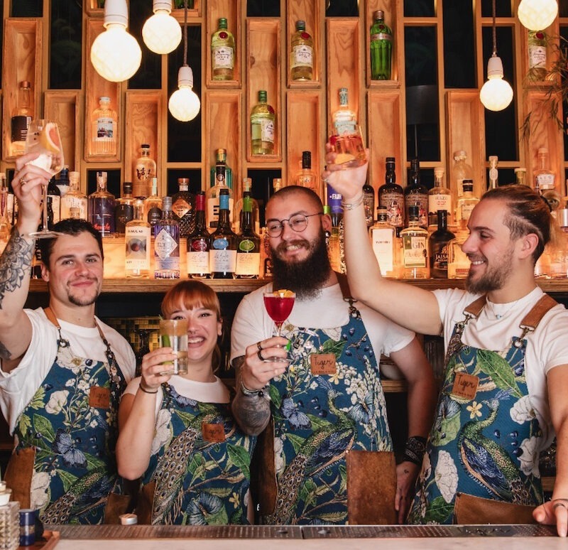 This is an image of a group of people behind a bar holding cocktails and smiling.