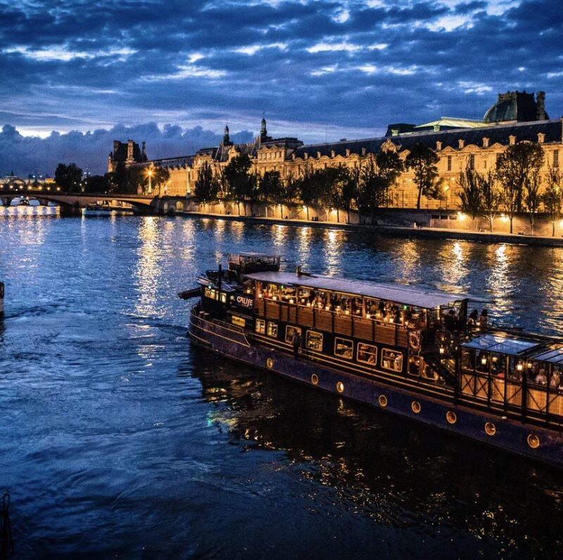 This is an image of a tour boat sailing through the Seine River. It is night, so there are lots of pretty lights.