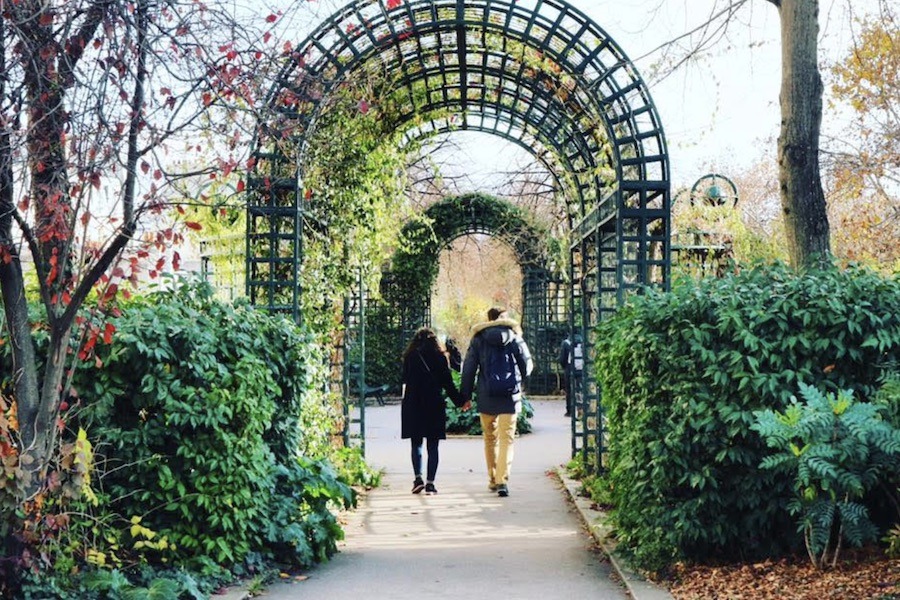 This is an image of two people walking hand in hand through a garden and little archway.