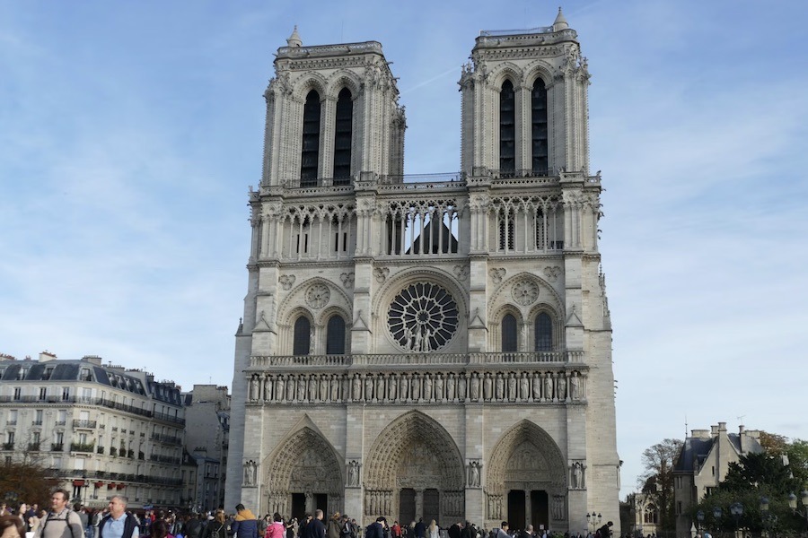 This is a picture of Notre-Dame Cathedral on a day with blue skies and people milling around the front.