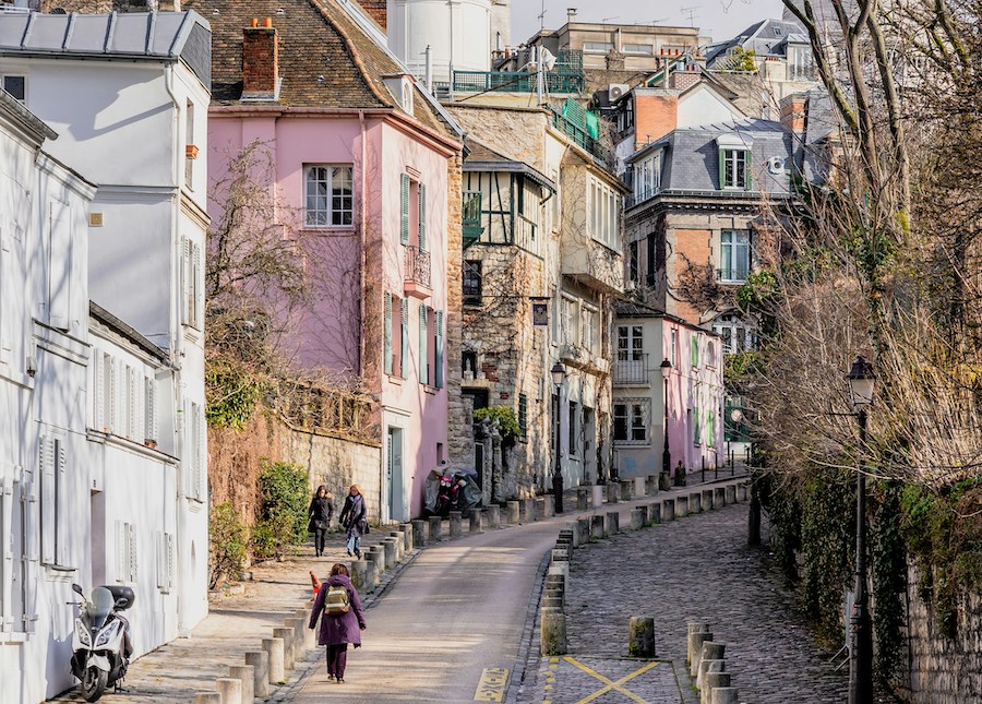 This is an image of a uphill cobblestone street in Paris with colourful houses lining it. There are a few people walking up. An important thing to know before visiting Paris is that the best way to see it is via walking, so bring appropriate footwear.