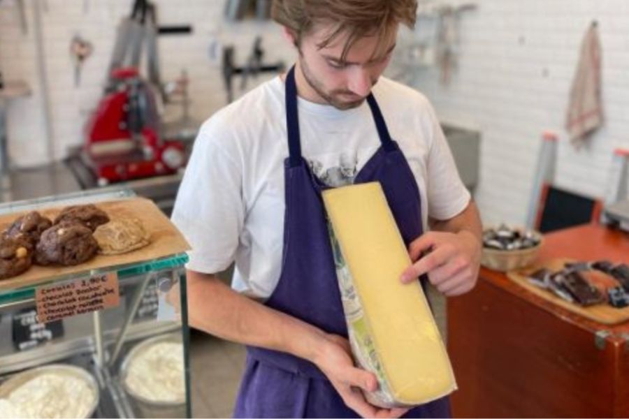 This is an image of a man pointing to a big block of cheese and explaining, what seems like, its origins and flavour profile.