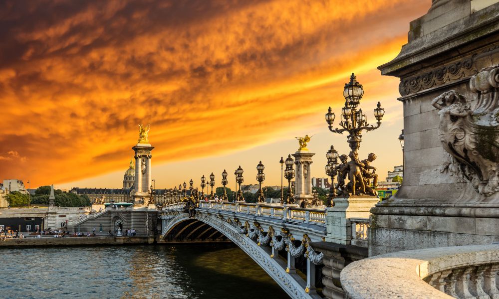 This is a picture of a famous Paris bridge that goes over the Seine. It is a great spot to watch the sunset on, as you can see the orange haze above it in this image.