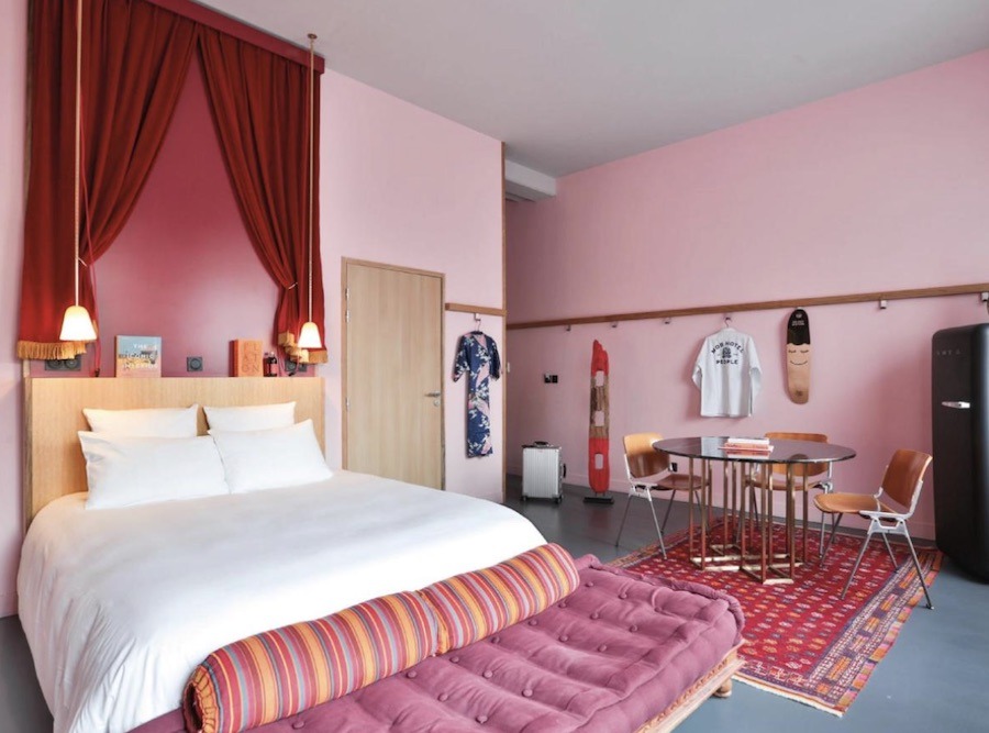 This is a picture of a hotel room that is full of pink decor from the walls to the rug and overhead draping. It looks very art-deco.