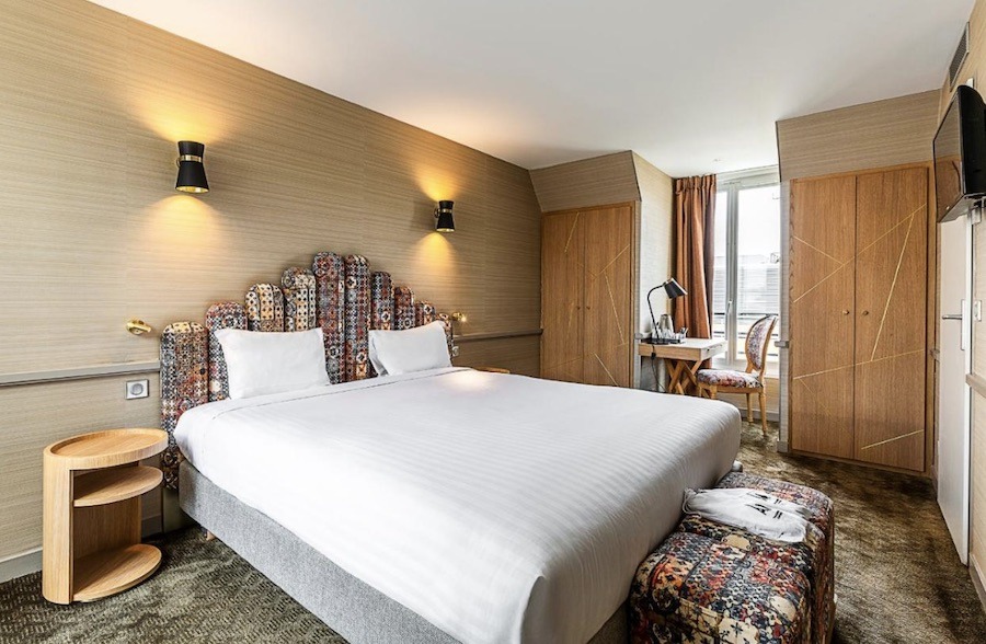 This is an image of a stylish hotel room. It has a double bed in the centre with a white duvet and a rainbow headboard with matching rainbow foot rests.