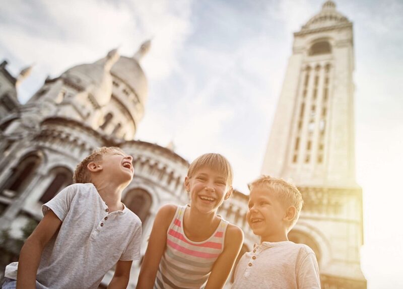 This is a picture of three kids laughing in front of the Sacre Coeur Cathedral.