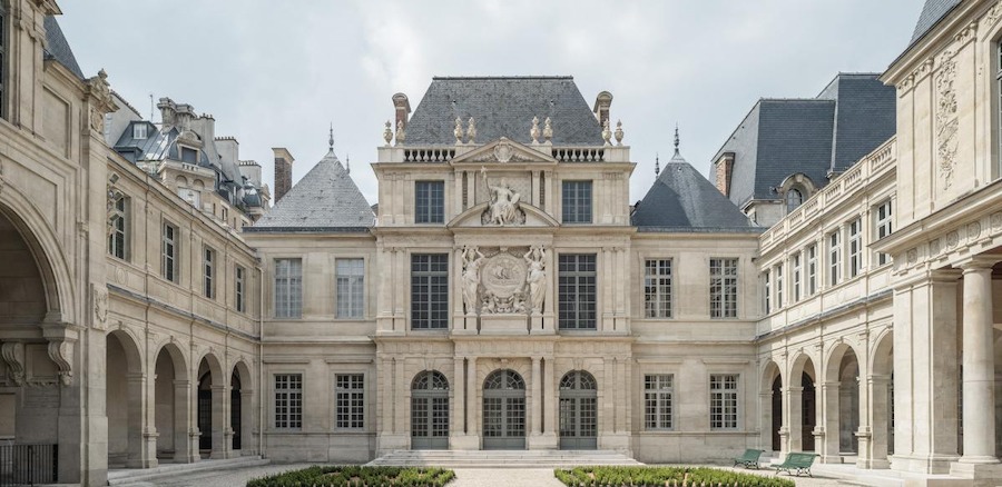 This is an image of the facade of a grand museum in Paris with stone light grey walls and a neat courtyard.