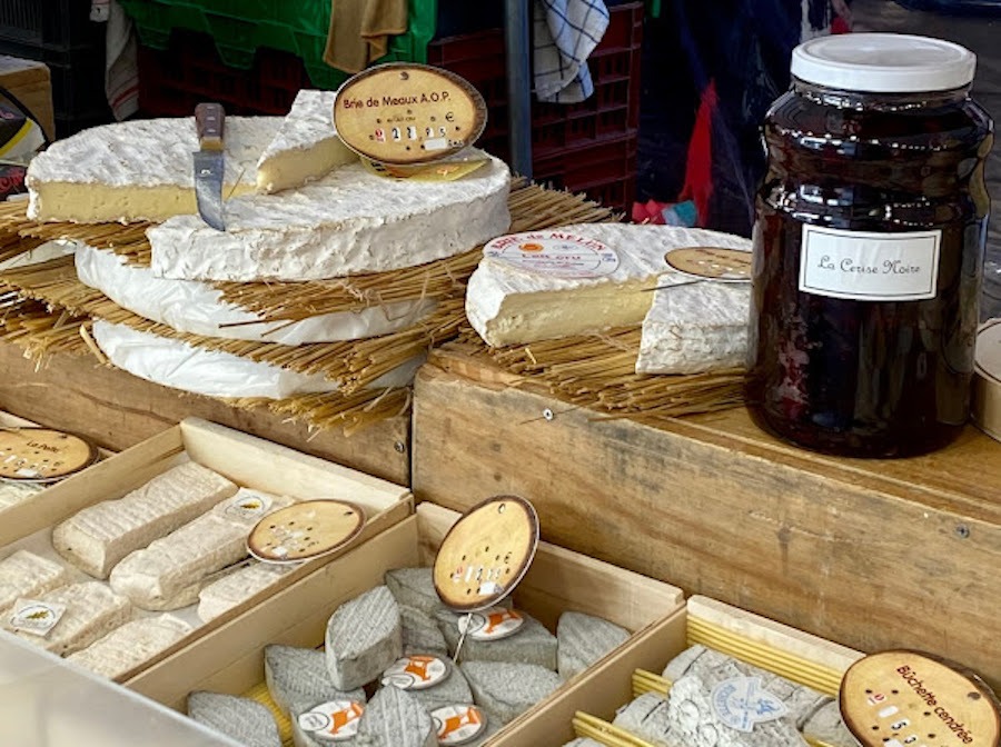This is an image of a large selection of soft cheeses. Some are individually wrapped, others remain as big cheese wheels that people can cut their own slices from.